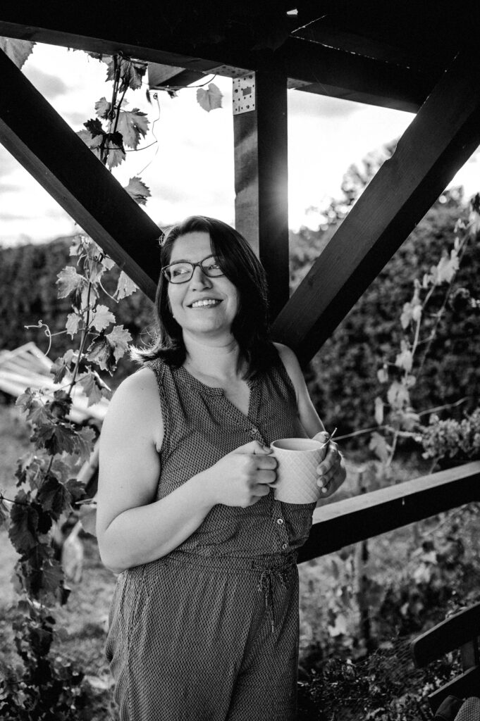 Kovács Marcsi újrakezdés mentor fekete-fehér portréja egy teraszon, mosolyogva a távolba néz.