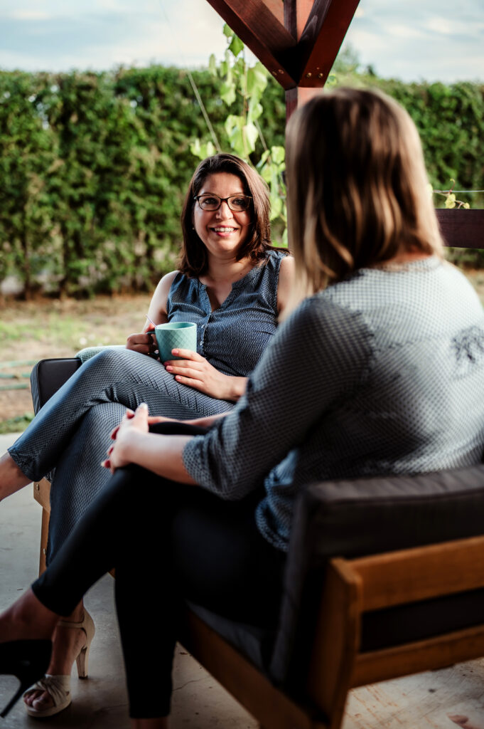 Kovács Marcsi mentor a teraszon ülve, figyelmesen és mosolyogva hallgatja kliensét egy egyéni konzultáció során.